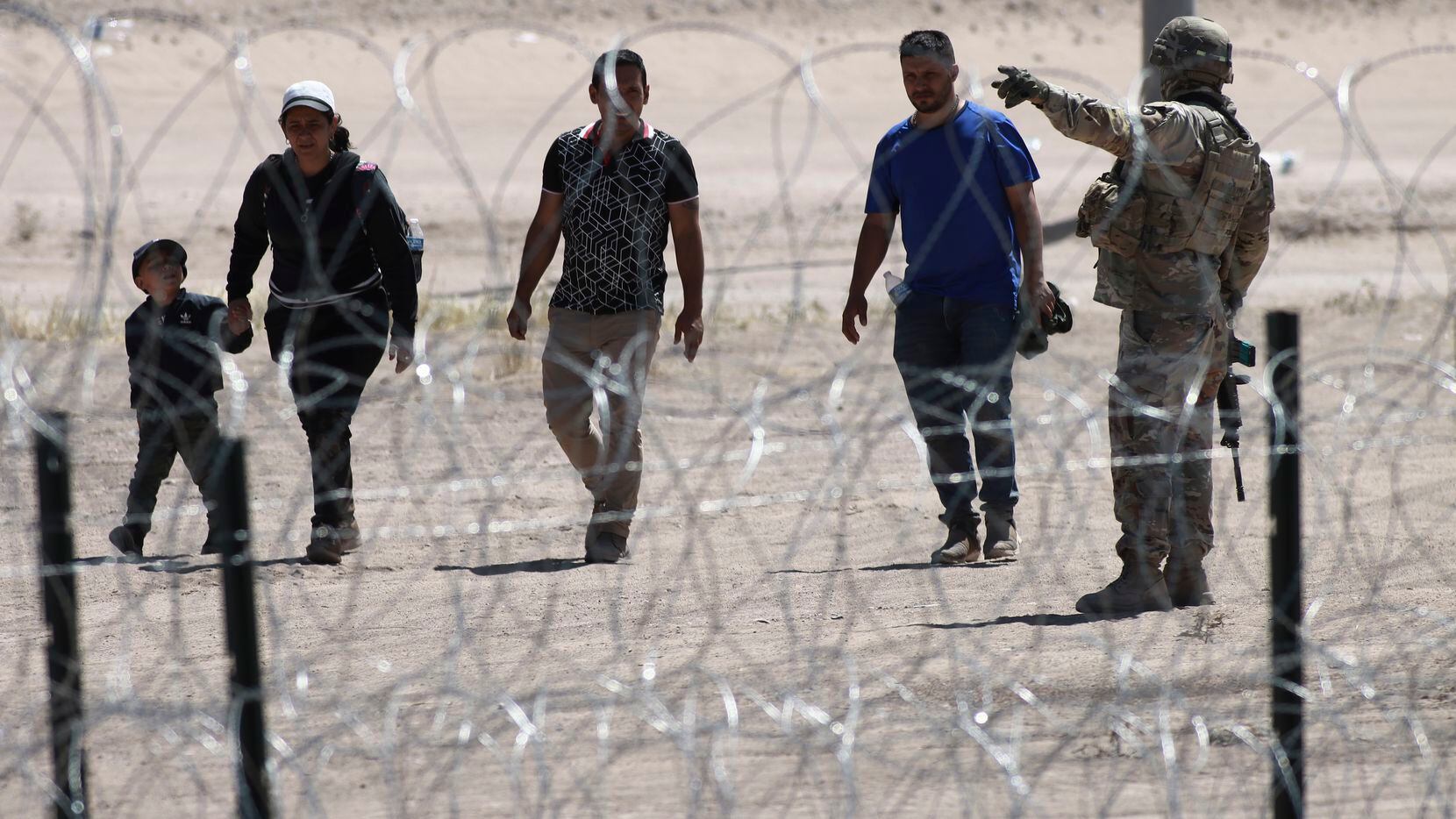 FILE - Migrants wait for U.S. authorities, between a barbed-wire barrier and the border...