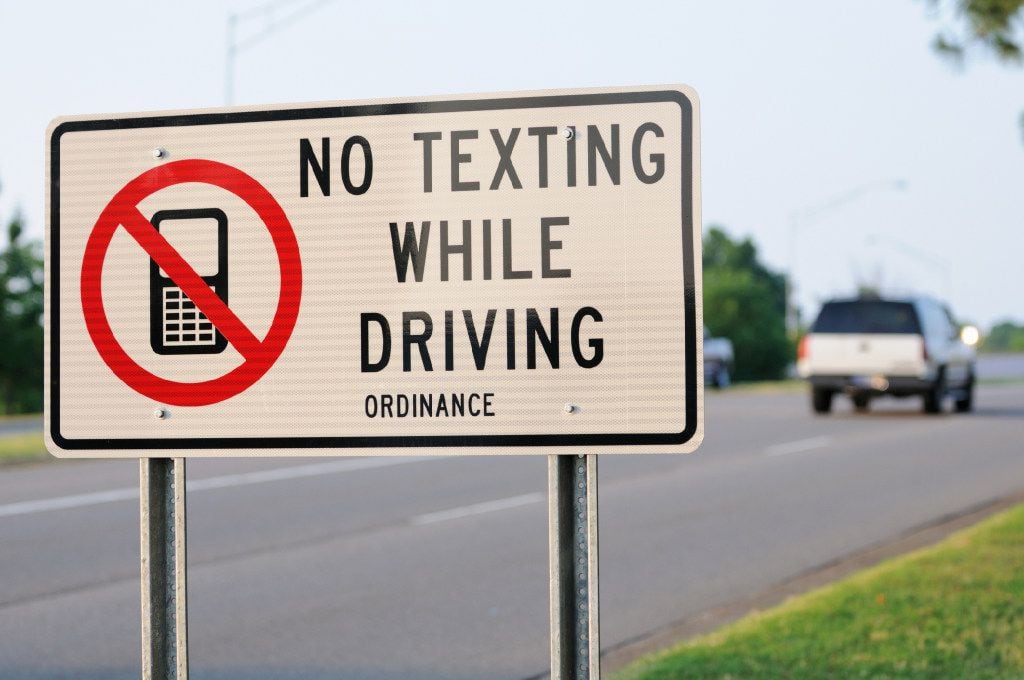 Close up of no texting while driving ordinance sign with vehicle in background.