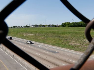 The chain link fence of a pedestrian bridge over LBJ Freeway frames undeveloped land on the...