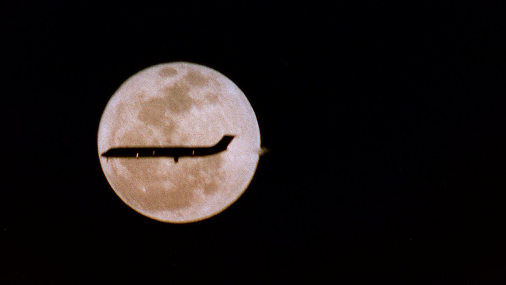 A full moon illuminates a plane's landing at DFW Airport.