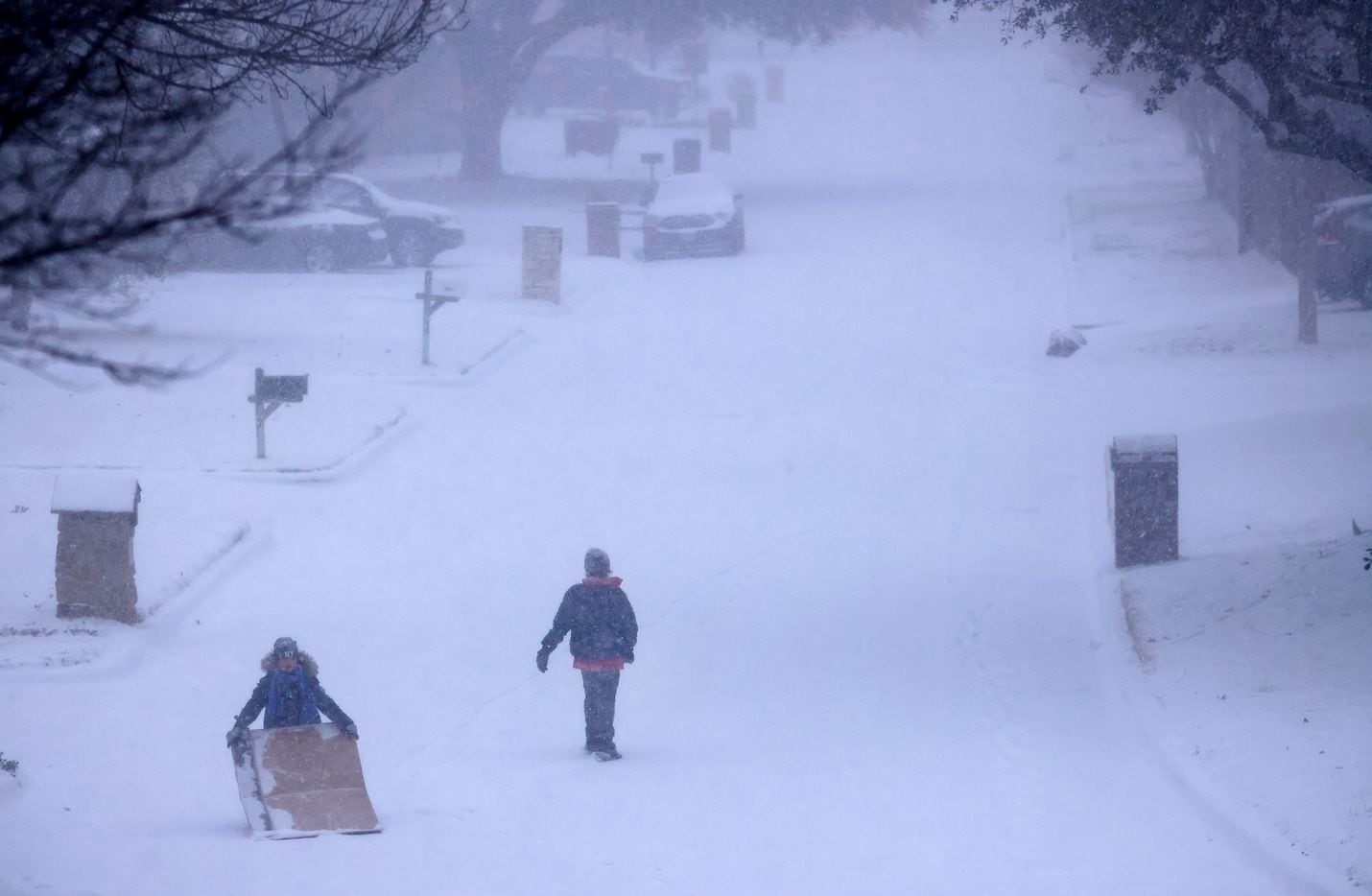 Kids improvised by sledding on large pieces of cardboard down a steep, snow-covered street...