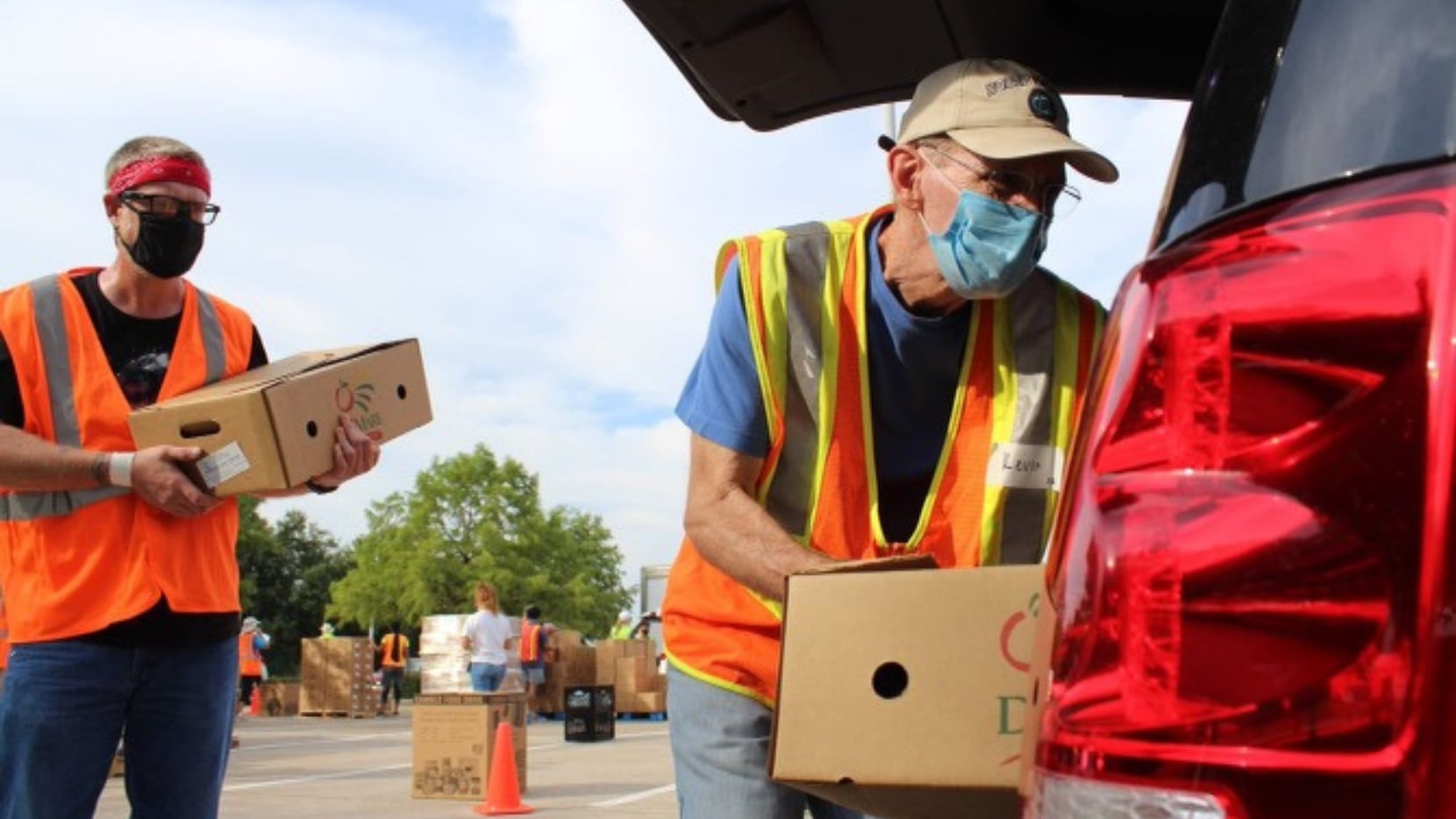 Two masked volunteers load boxes into the trunk of a car as part of Nourish North Texas.