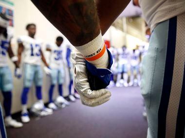 Dallas Cowboys running back Ezekiel Elliott (blue glove) joins hands with teammates as they...