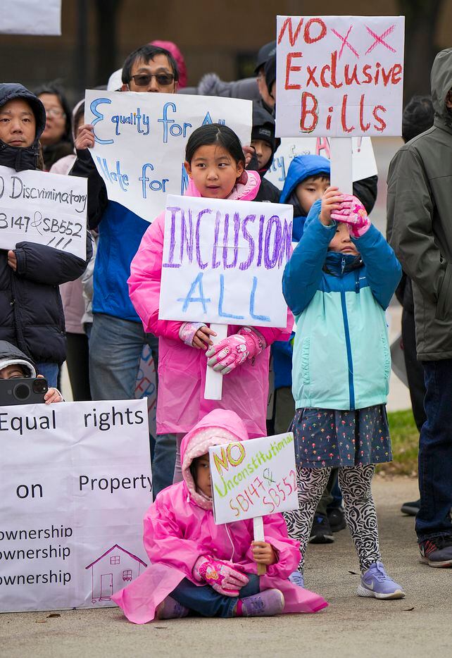 Aima Zheng, 9, (center) holds signs with her sisters Anna, 6, (bottom) and Aya 5 (right), ...