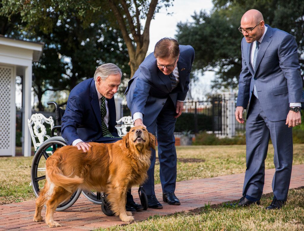Gov. Greg Abbott (left) and House Speaker Dennis Bonnen pet one of the governor's dogs,...