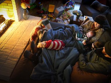 Dan Bryant and his wife Anna watch "Frozen" by the fire with sons Benny, 3, and Sam, 12 weeks, along with their dog Joey, also wearing two doggie sweaters, with power out and temperatures dropping inside their home after a winter storm brought snow and freezing temperatures to North Texas on Monday, Feb. 15, 2021, in Garland.  The Bryant’s, who lost power Monday morning, were wearing outdoor winter clothes, down to snow boots, hat, and ski pants, and even their dog Joey had two doggie sweaters.