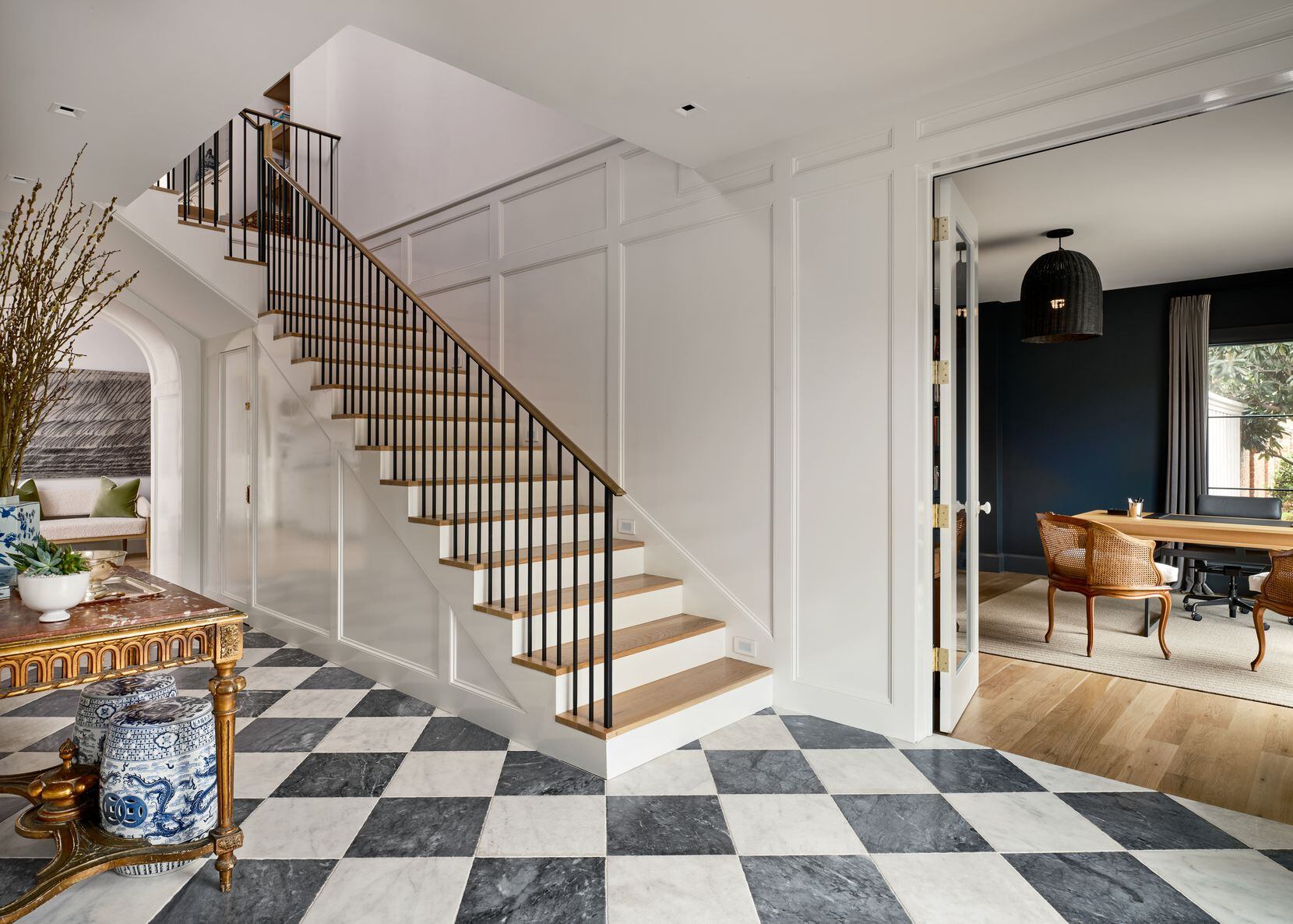 An entry features black-and-white checkered floors, an antique table, and white lacquered...
