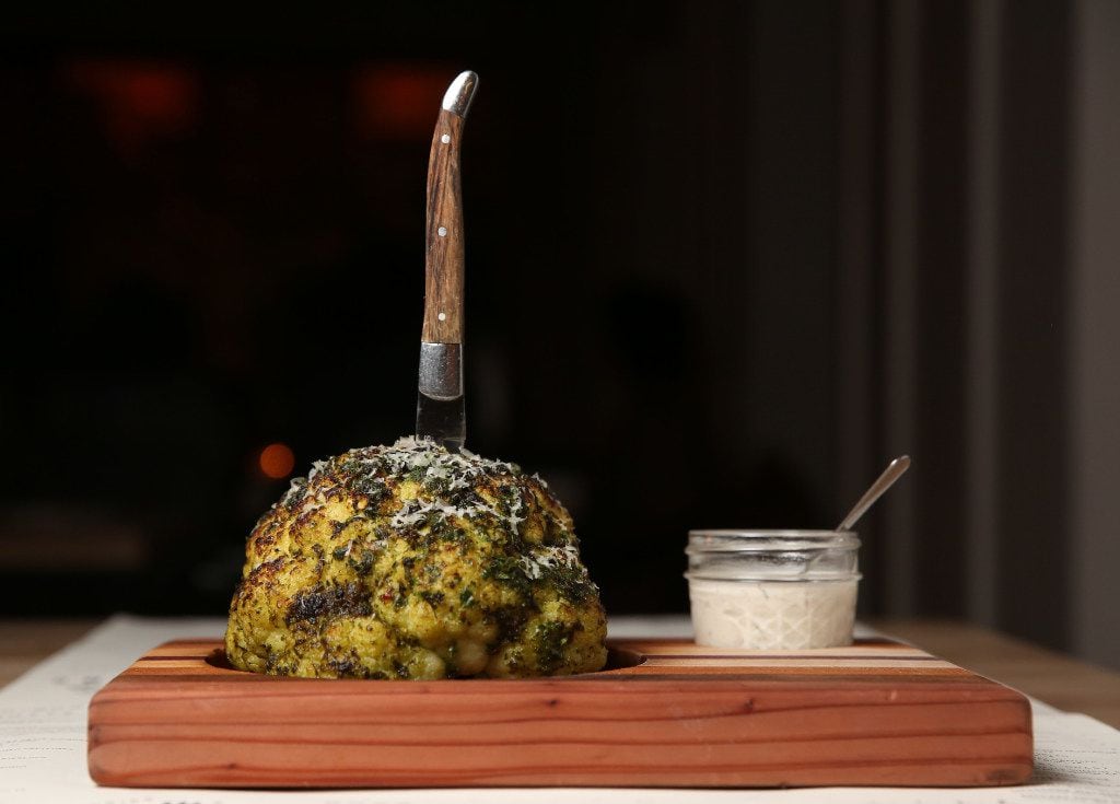 A pesto-encrusted roasted cauliflower looks like a brain on a board, stabbed with a knife.