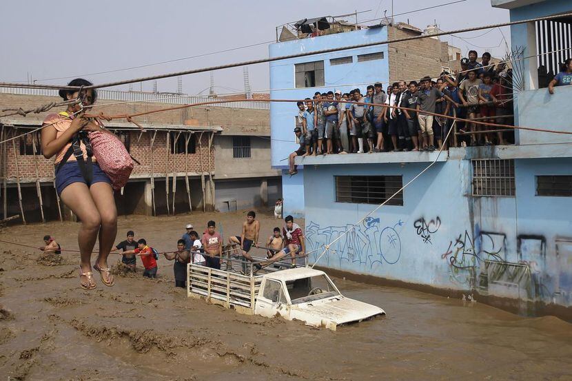 Una mujer es jalada hacia un lugar seguro mediante una cuerda en Lima, Perú. Las lluvias y...