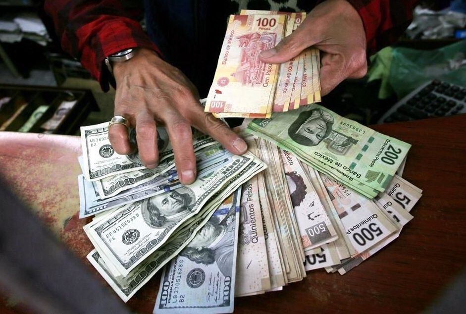 Un empleado de una casa de cambio entrega dólares estadounidenses y pesos mexicanos enviados...