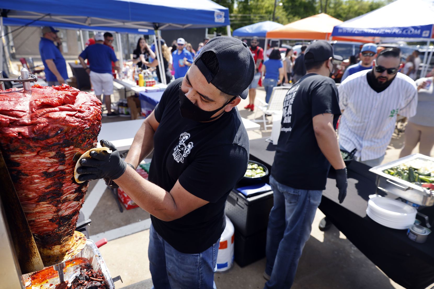 Saul Hernandez trims pork shoulder for Trumpo during an Opening Day tailgate party on private property outside of Globe Life Field in Arlington, Monday, April 5, 2021. The Rangers are facing the Toronto Blue Jays in the home opener. (Tom Fox/The Dallas Morning News)