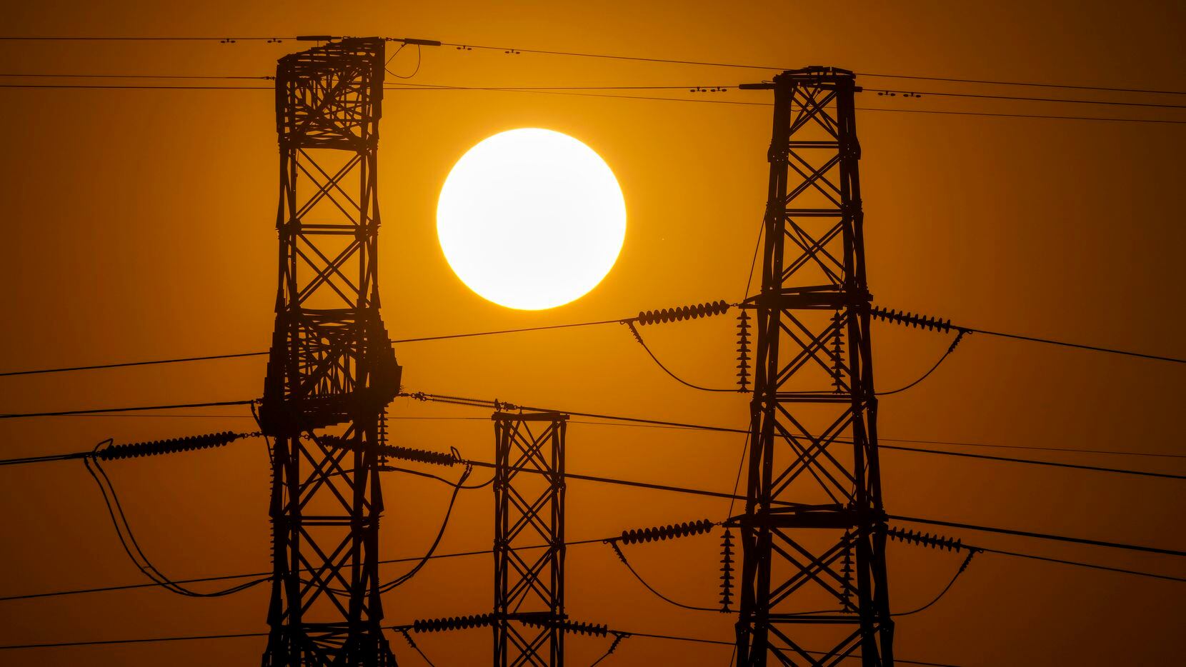 The sun sets behind power lines near Mountain Creek Lake on Monday, July 11, 2022, in Dallas.