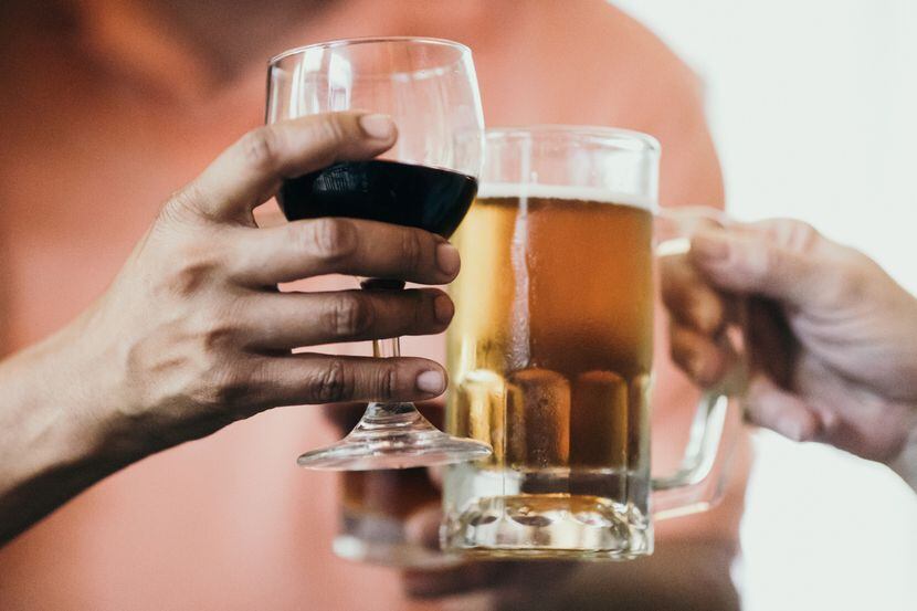Dos personas brindan con una copa de vino y tarro de cerveza.