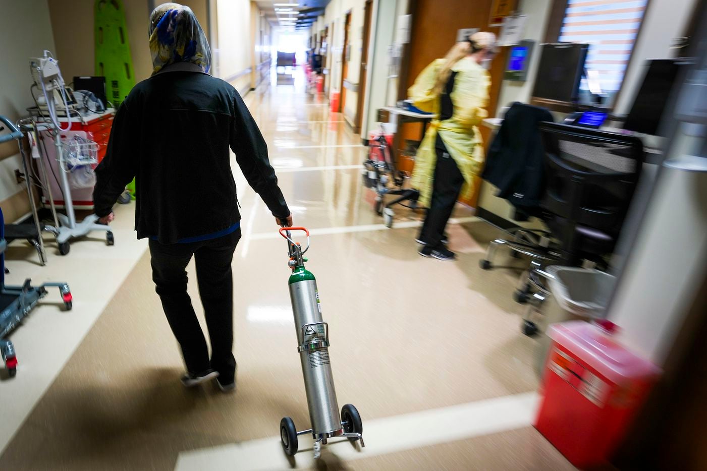 Fara Ajani, associate manager in medicine services, pulls an oxygen cylinder down a hallway...