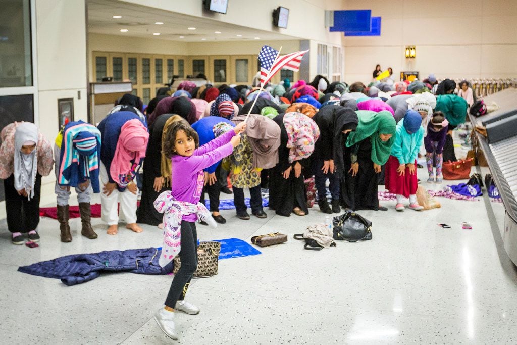 A young girl waves the American flag as Muslim women set down their protest signs to pray at...