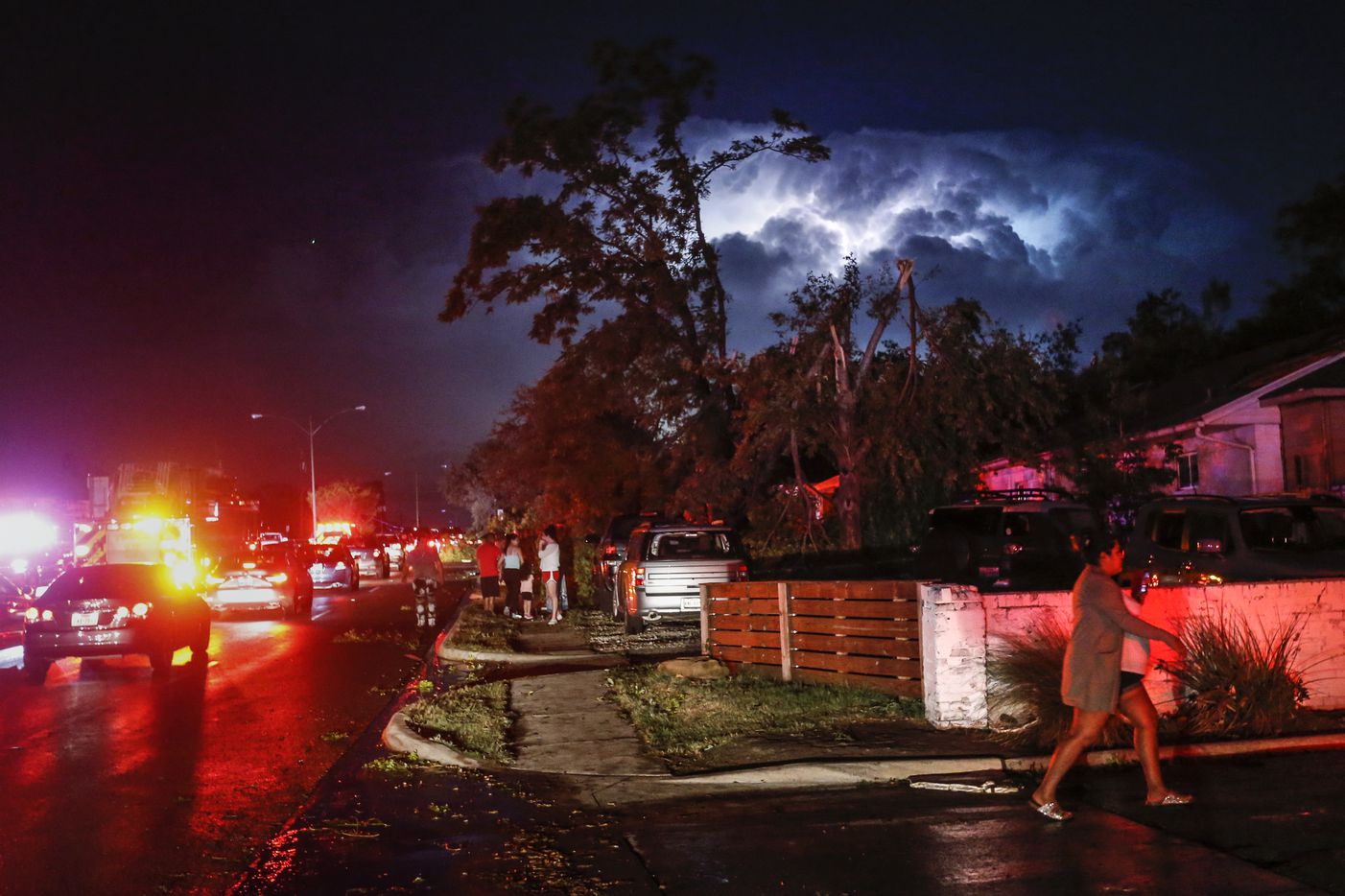Lightning and emergency lights highlight damage as people gather in the parking lot of a shopping complex near the intersection of Walnut Hill Lane and Marsh Lane in Dallas where a tornado hit Sunday, Oct. 20, 2019.
