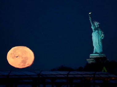 The supermoon appears near the Statue of Liberty, Monday, Nov. 14, 2016, in New York. Monday's supermoon, a phenomenon that happens when the moon makes a close pass at the earth, is the closest to earth since 1948.
