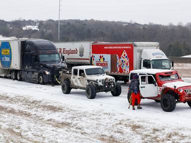 Members of the Carnales Off Road Jeep club work to pull a semi-truck up an ice covered hill...