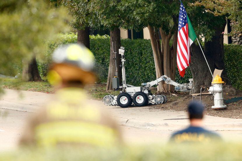 A suspicious package is pulled out of the bushes by a police robot in front of the...