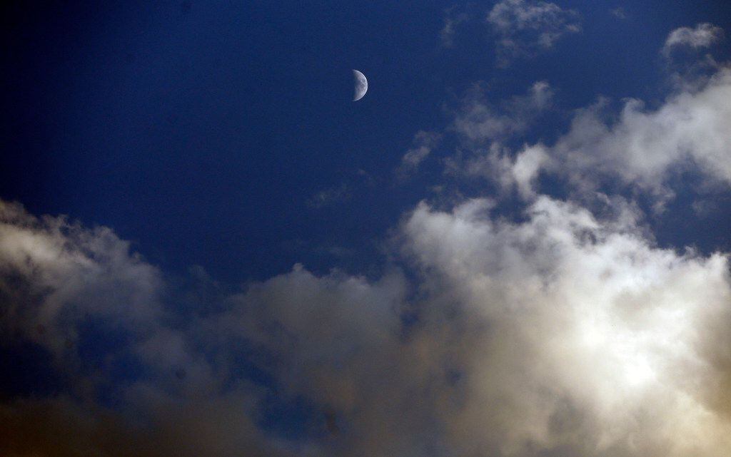 The moon still shines among late-afternoon clouds, during a 30-minute lightning delay before...