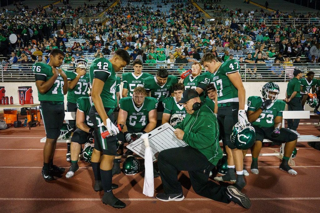 Arlington offensive linemen huddle with a coabh during the first half of a high school...