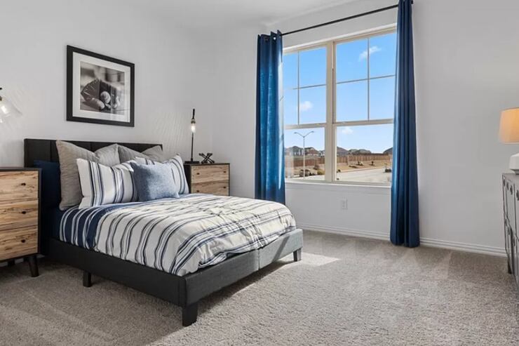Bedroom with striped bedspread, wood-faced nighstands and blue curtains pulled back to show...