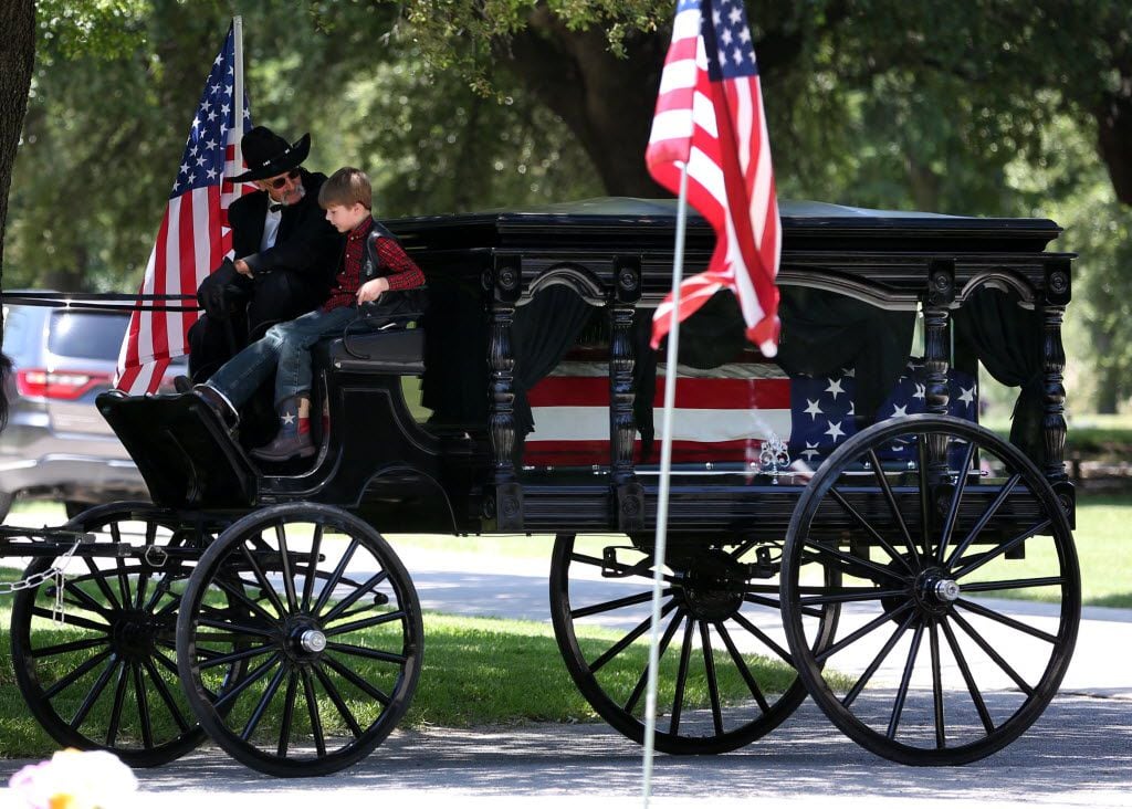 Magnus Ahrens, 8, son of fallen Dallas police Senior Cpl. Lorne Ahrens sits with the driver of a caisson bearing his father's casket during Ahrens' burial service. 