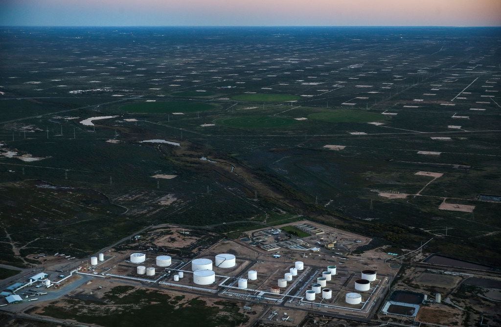 An oil tank farm is seen in the foreground of a pumpjack speckled production field, just...