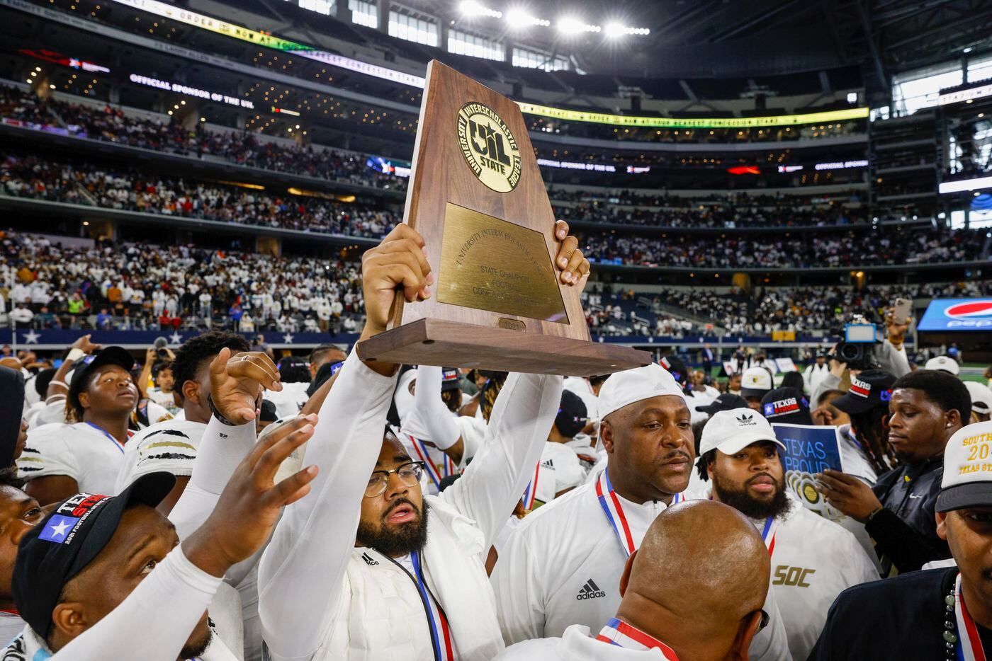 South Oak Cliff assistant coach Domenic Spencer raises the championship trophy after the Class 5A Division II state championship game at AT&T Stadium in Arlington, Saturday, Dec. 18, 2021. South Oak Cliff defeated Liberty Hill 23-14 for Dallas ISD’s first title since 1958. (Elias Valverde II/The Dallas Morning News)