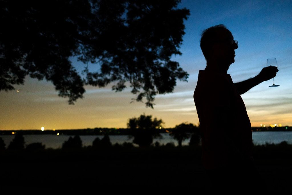 Zoltan Zsohar has a glass of wine as he gathers with neighbors to watch the sun set from the front yard of his home overlooking White Rock Lake on Thursday, Aug. 8, 2019, in Dallas. (Smiley N. Pool/The Dallas Morning News)