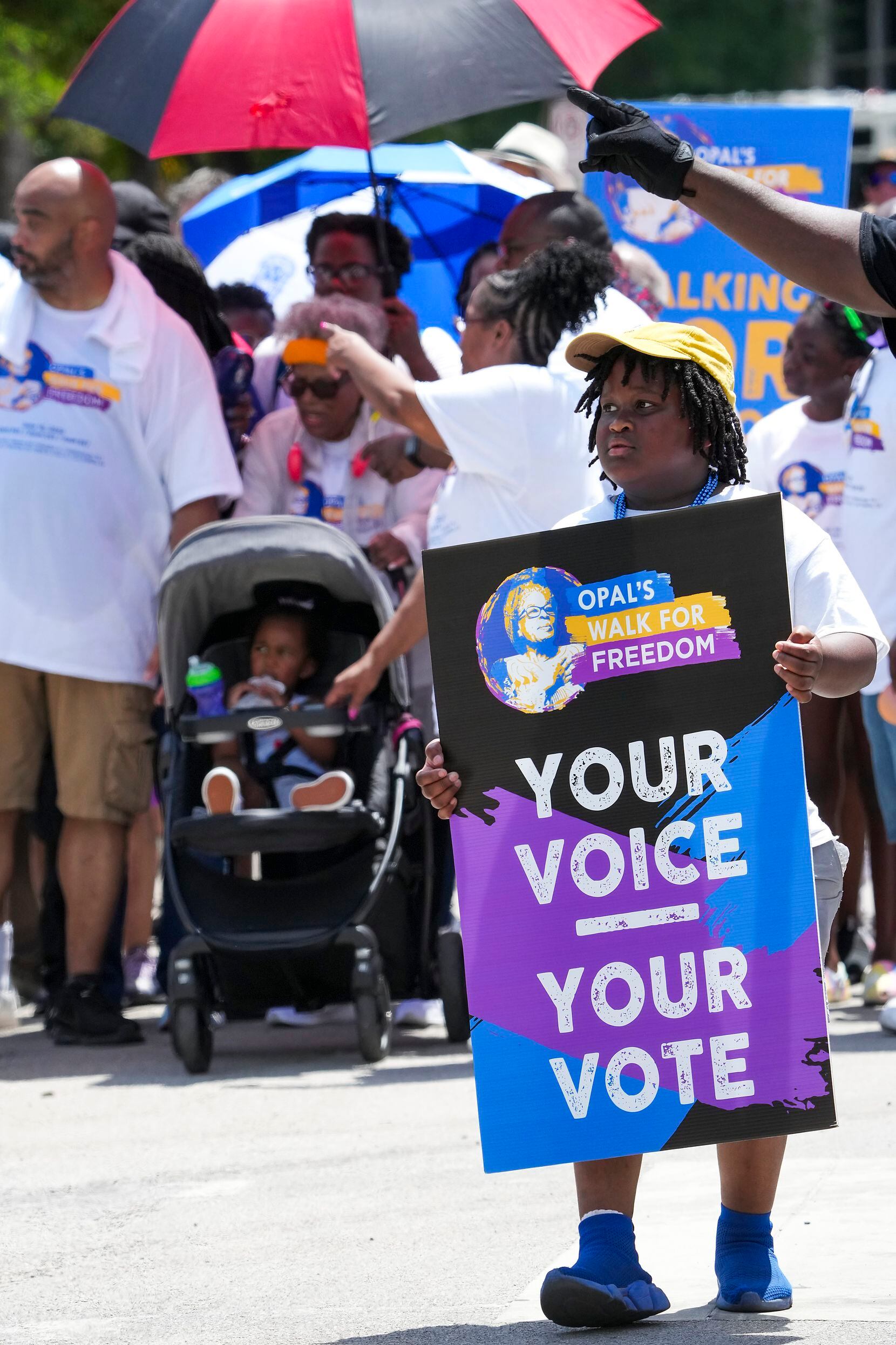 Brandyn Harris carries a sign supporting voting as Opal Lee pushes one of her great...
