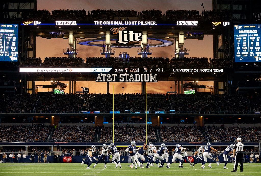 FILE - The sunset is seen through the open end-zone doors at AT&T Stadium as the Cowboys run a play during a game against the L.A. Rams in Arlington on Sunday, Dec. 15, 2019.