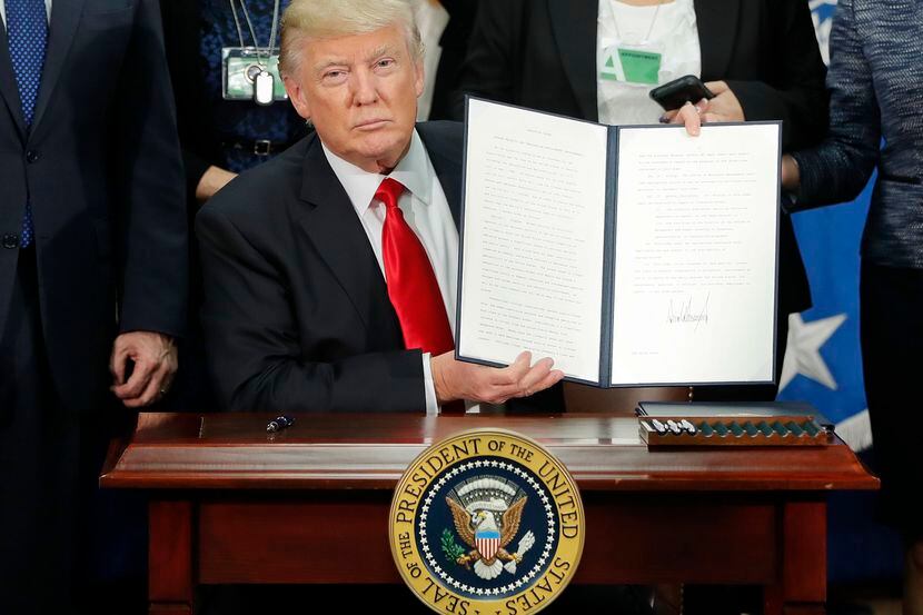El presidente Donald Trump sostiene el documento de orden ejecutiva respecto a reforzamiento...