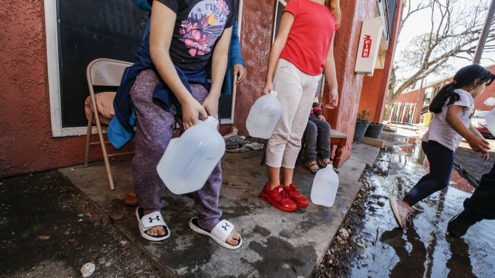 Alina Mendoza, 6, and Deveany Mendoza, 10, carry jugs of water into their apartment at the...