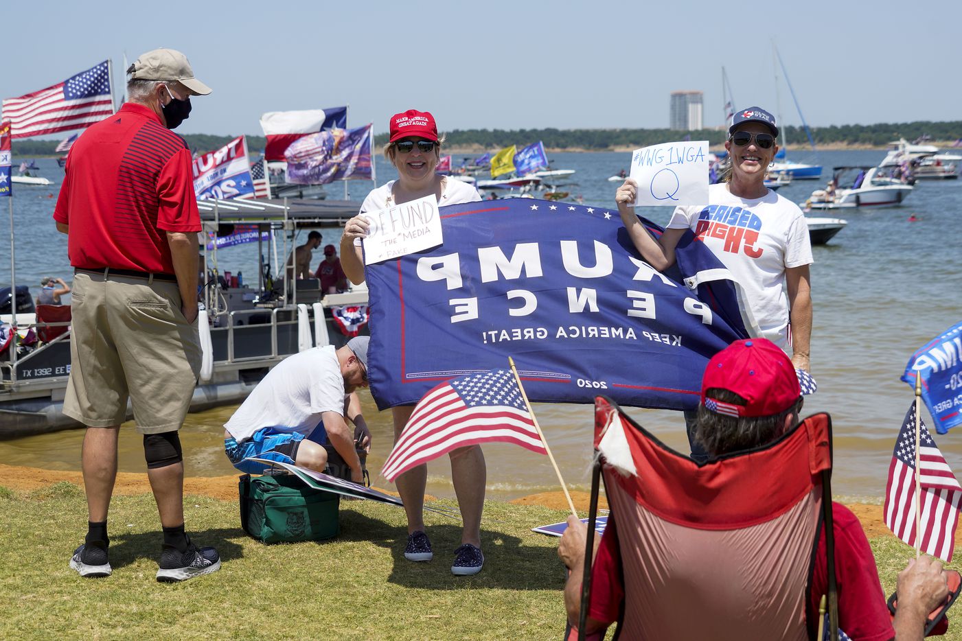 Supporters of President Donald Trump pose for photos holding signs in support of QAnon, and in opposition to the media, during a campaign rally and boat parade at Oak Grove Park on Grapevine Lake on Saturday, Aug. 15, 2020.
