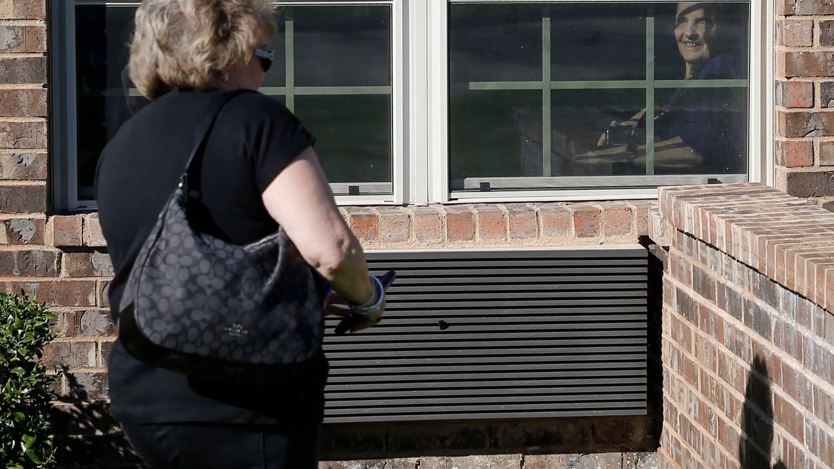 Cindy Goleman walks up to the window of her mother Peggy White from outside the window at...