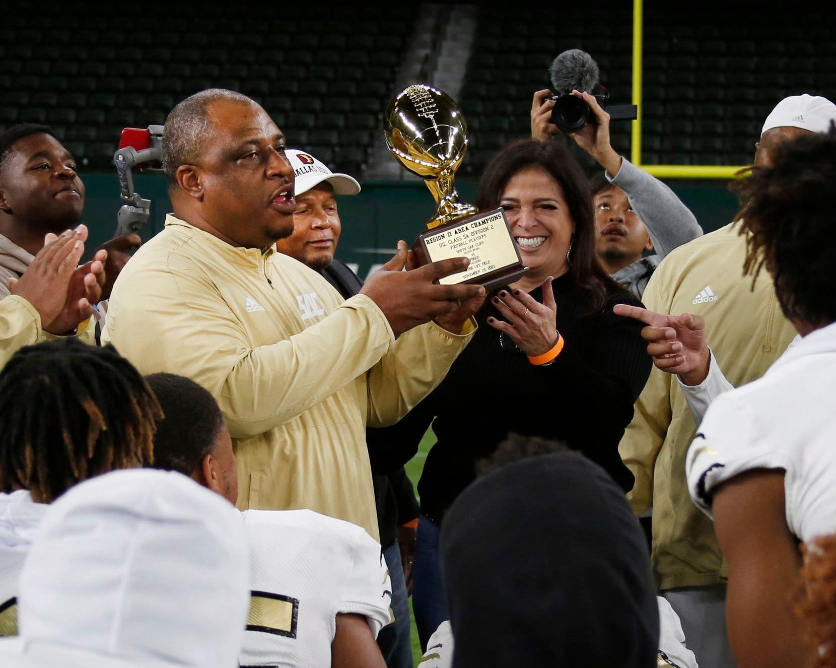 South Oak Cliff head coach Jason Todd raises the Region ll Area Champions trophy after presented by Dallas ISD Athletics Director Dr. Sylvia Salinas. The Golden Bears of South Oak Cliff defeated Frisco 35-24 to advance. The two teams played their Class 5A Division ll area-round playoff football game at Globe Life Field in  Arlington on November 18, 2021. (Steve Hamm/ Special Contributor)