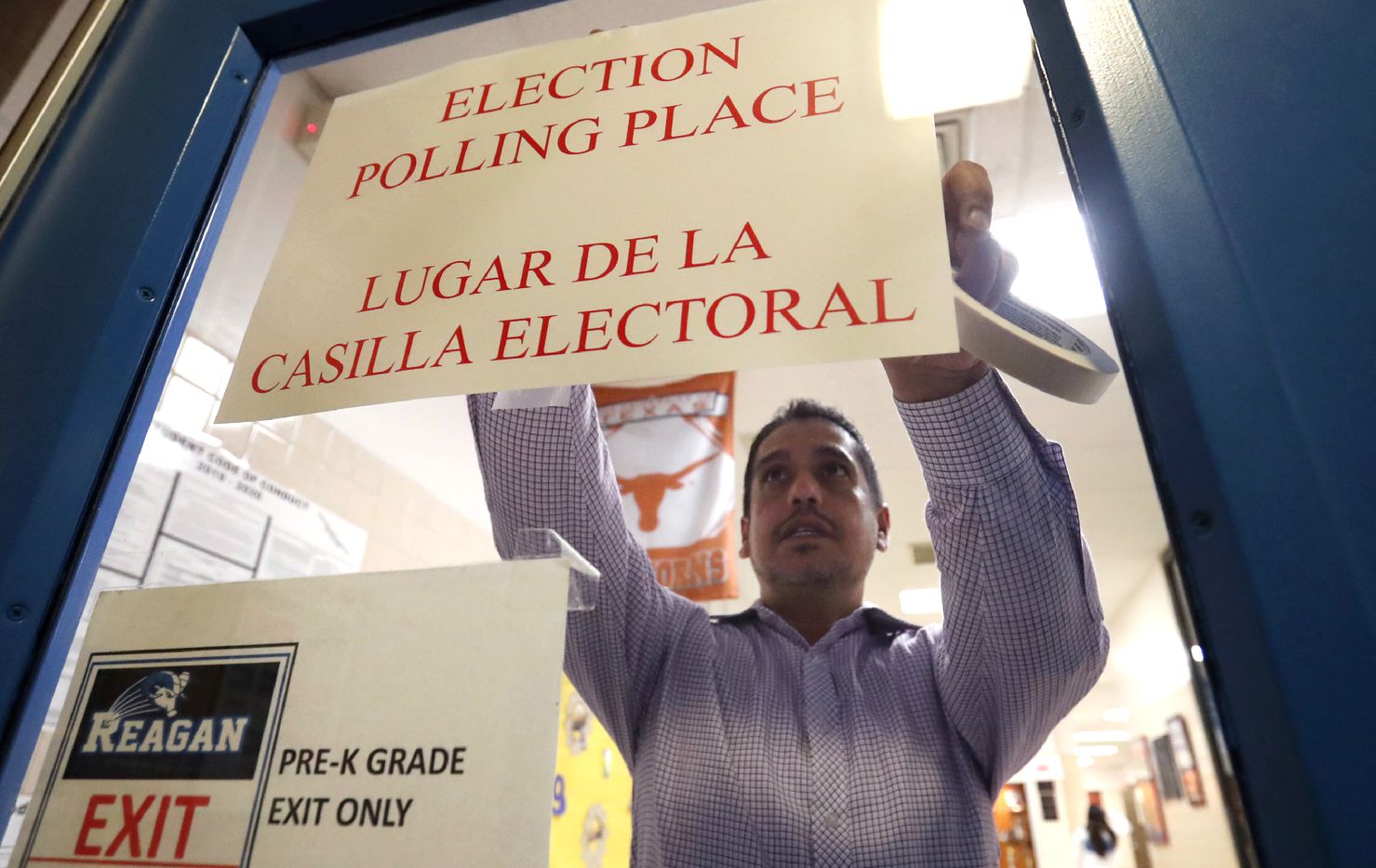 Dallas County election worker Maxx Nunez tapes up a sign before polls open for Super Tuesday voting at John H. Reagan Elementary School in the Oak Cliff section of Dallas, Tuesday, March 3, 2020.