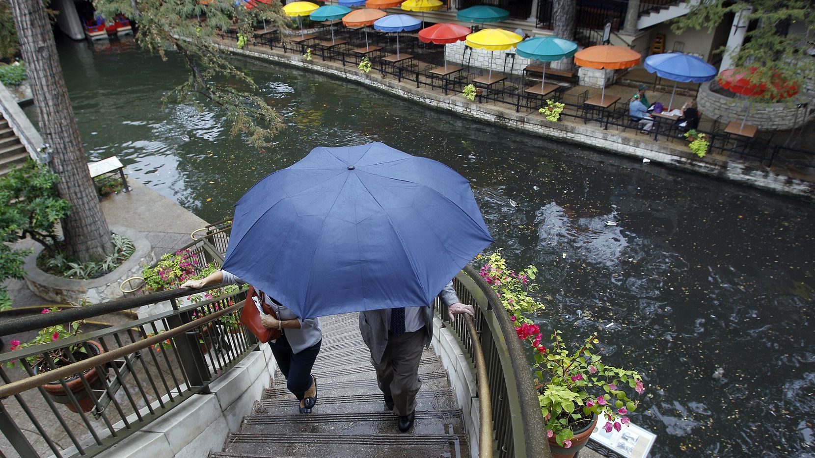 Visitors use an umbrella for protection from a light rain as they walk along the River Walk,...