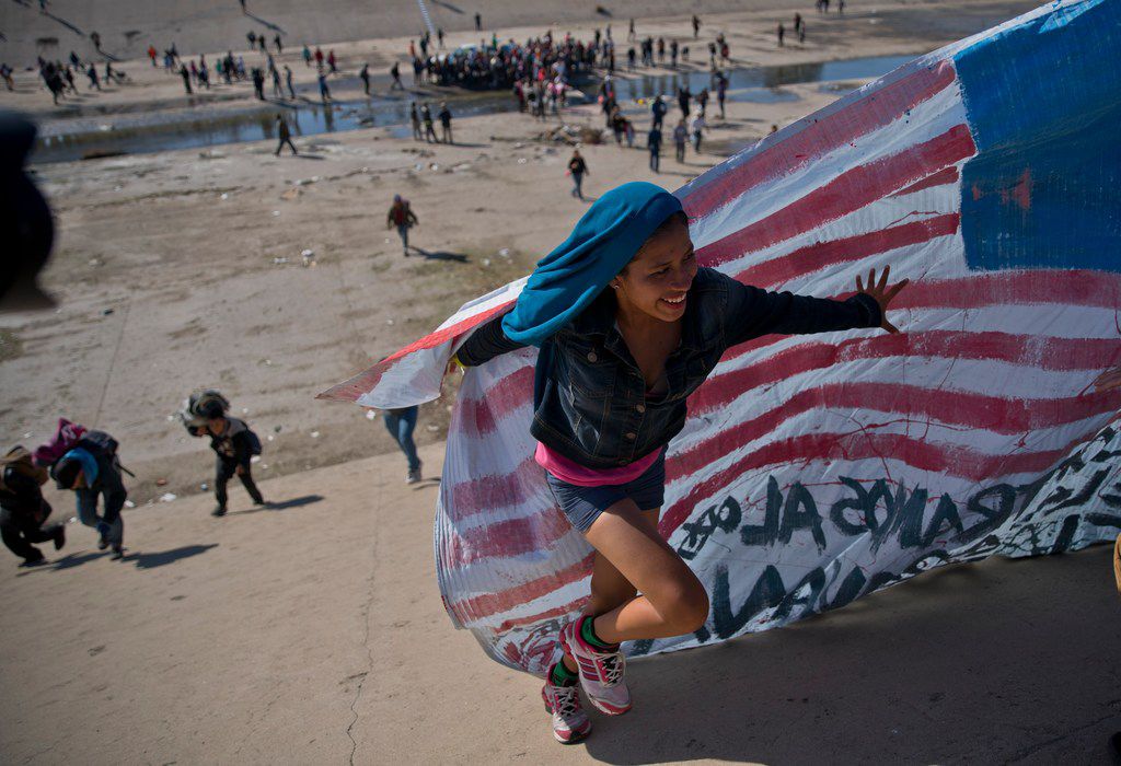A migrant woman helps carry a handmade U.S. flag up the riverbank at the Mexico-U.S. border...