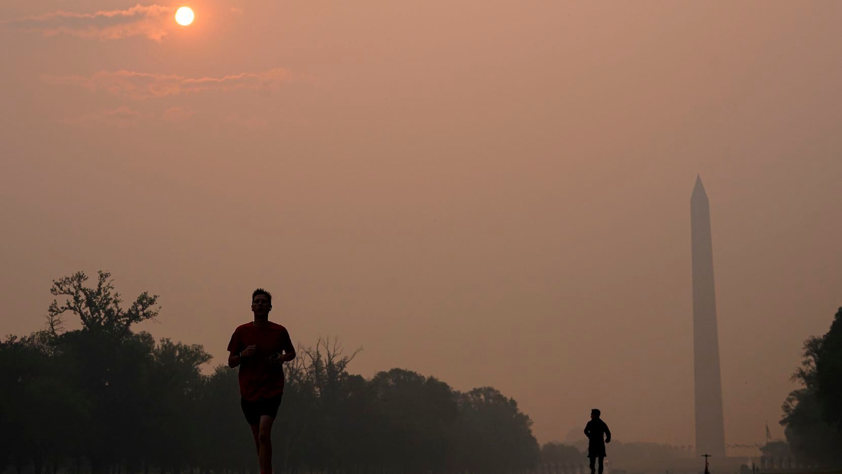 Joggers trot along the Reflecting Pool with the sun rising over the Washington Memorial and...