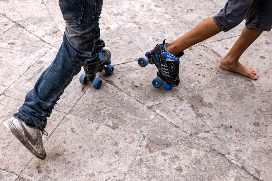 A Guatemalan boy and a El Salvadoran boy share a pair of roller skates in a gazebo in a...