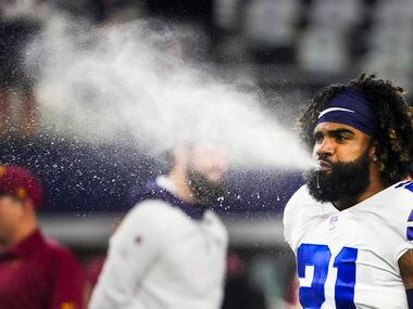 Dallas Cowboys running back Ezekiel Elliott blows water while warming up before an NFL...