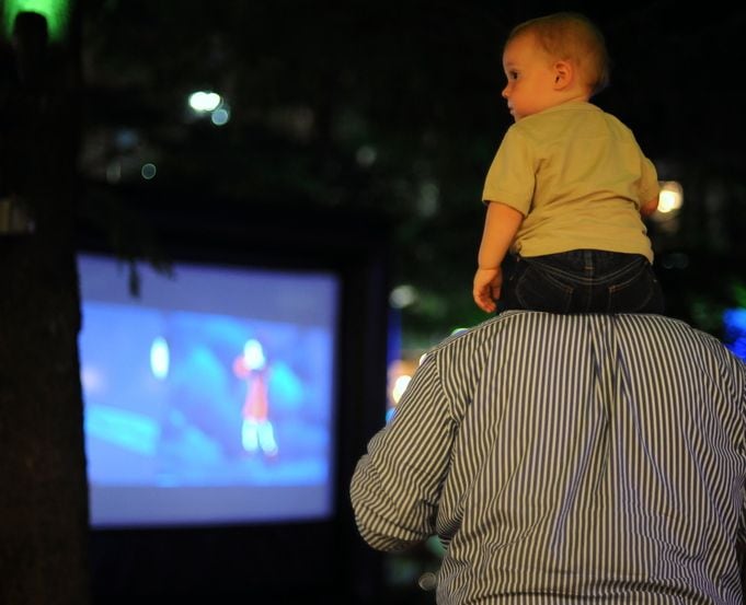 A boy sits on his dad's shoulders during an outdoor movie screening.
