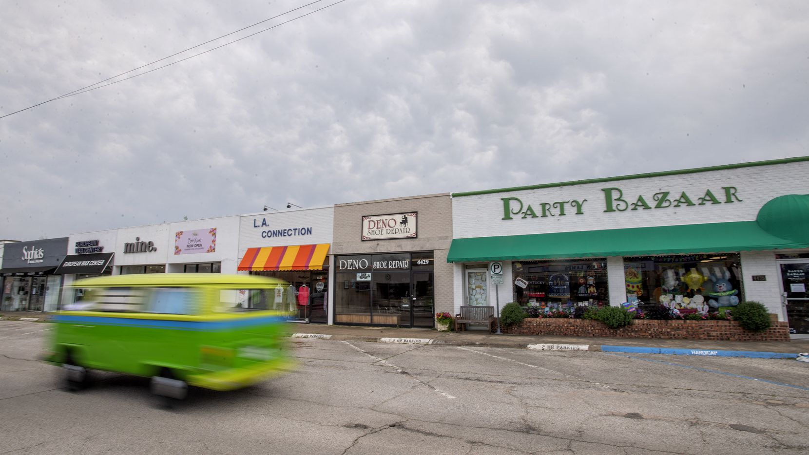A brightly painted Volkswagen bus drives past shuttered small businesses near Lovers Lane...