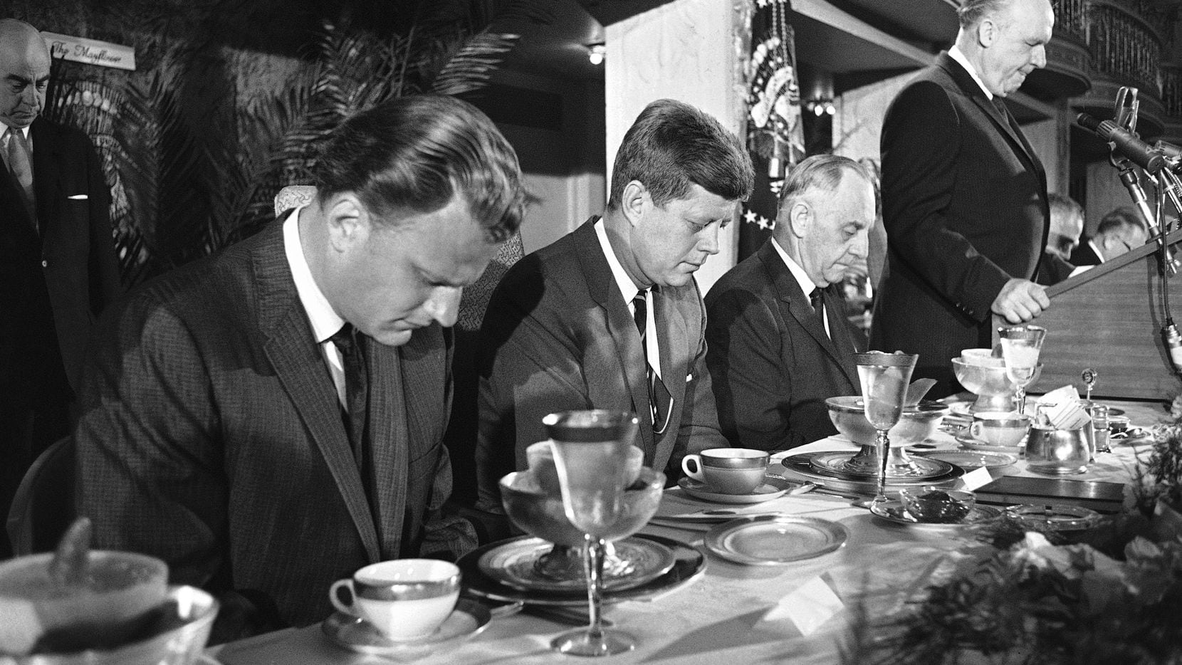 President John F. Kennedy and others at the head table bow their heads during the invocation...
