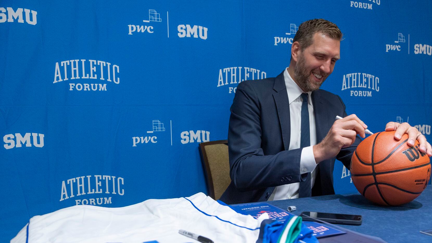 Former Dallas Mavericks player Dirk Nowitzki autographs a basketball before speaking at the...