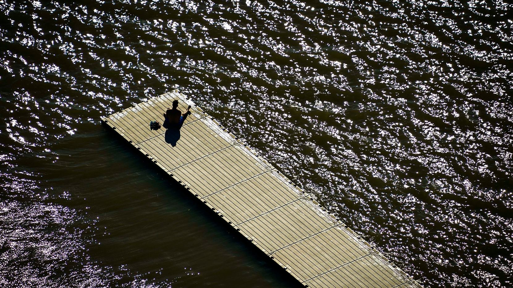 A man sits alone on a boat dock at White Rock Lake in Dallas on Tuesday, March 24, 2020.