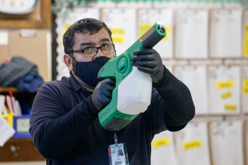 El conserje Joe Gómez rocía desinfectante en un salón de clases en la Academia STEAM Rayburn...