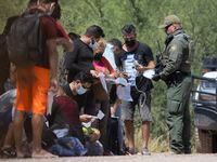A group of mostly Cuban migrants are handed bags for their belongings by Border Patrol...